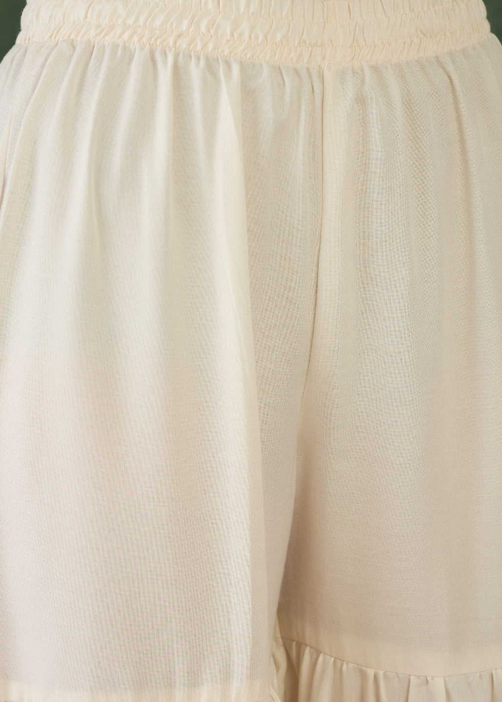 Close-up of beige pants with a textured top section on a plain background