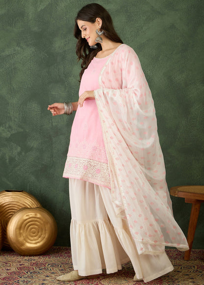 Woman in a pink and white traditional outfit against a green wall.