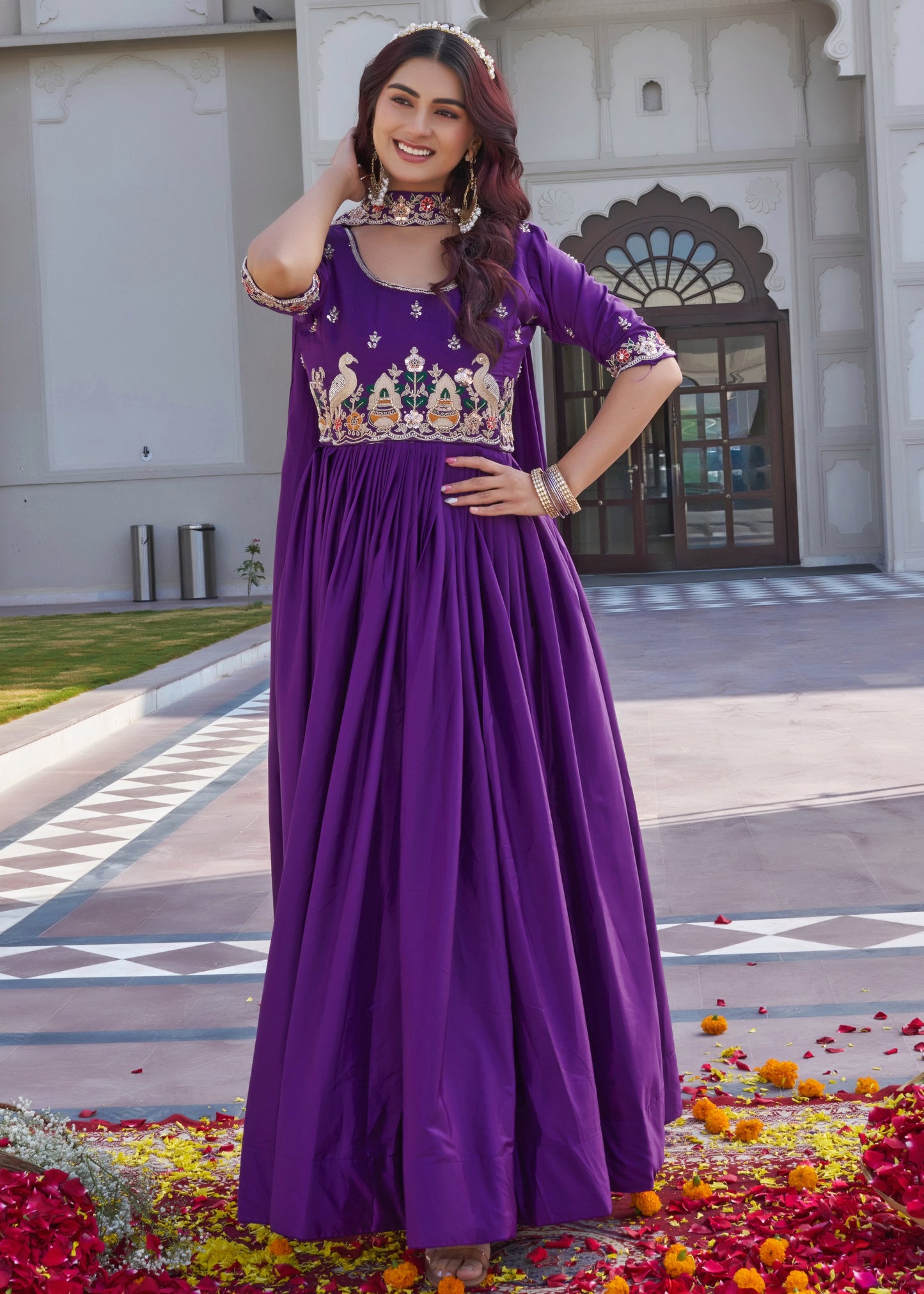 Woman in a purple traditional outfit standing in front of a building with decorative elements.