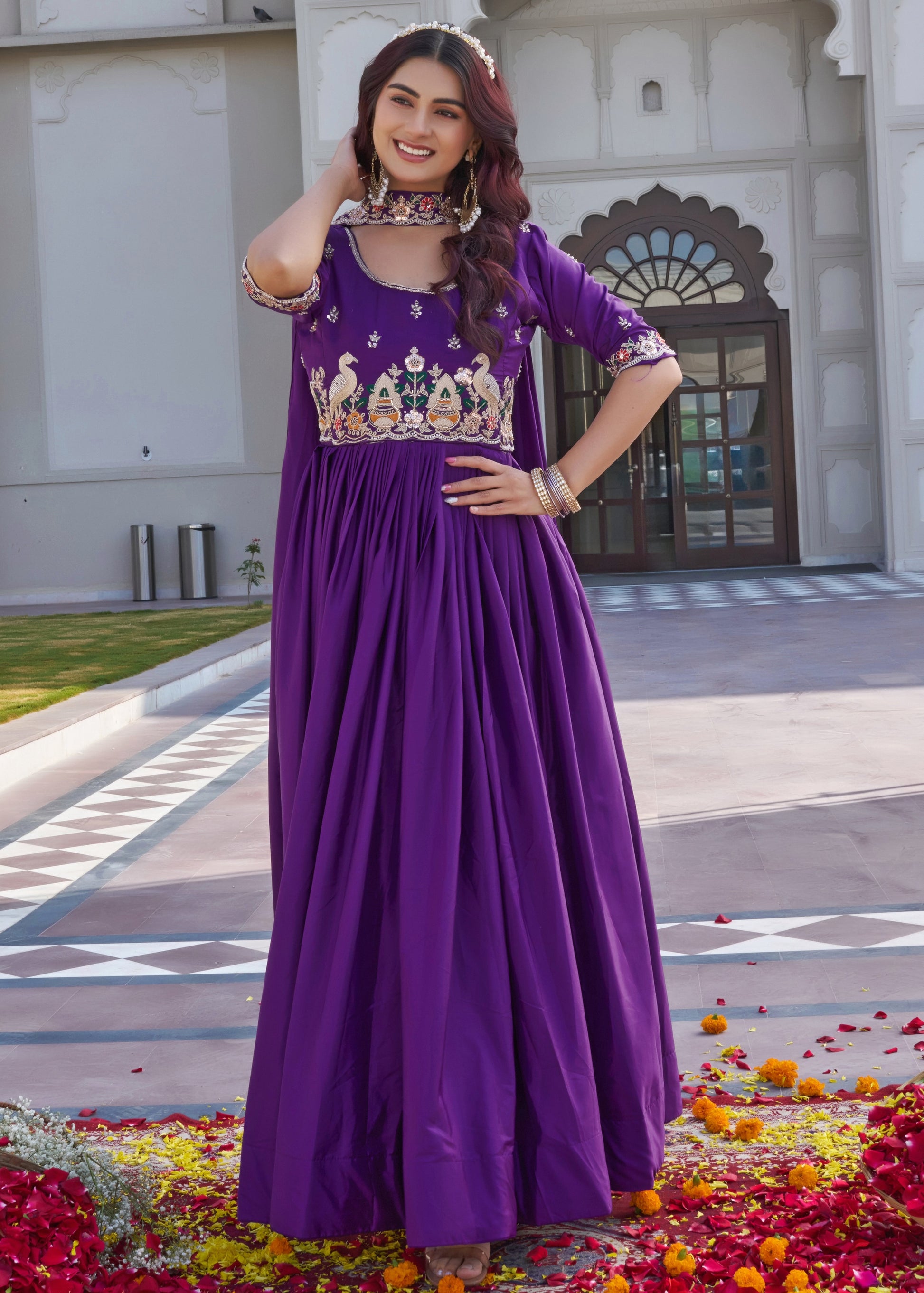 Woman in a purple traditional outfit standing in front of a building with decorative elements.