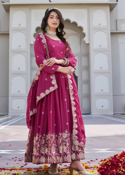 Woman in a pink traditional outfit standing in front of a building with floral decorations on the ground.